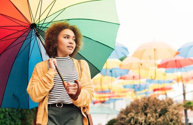 Mujer sonriente dando un paseo al aire libre con un paraguas de arco iris