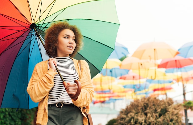 Mujer sonriente dando un paseo al aire libre con un paraguas de arco iris