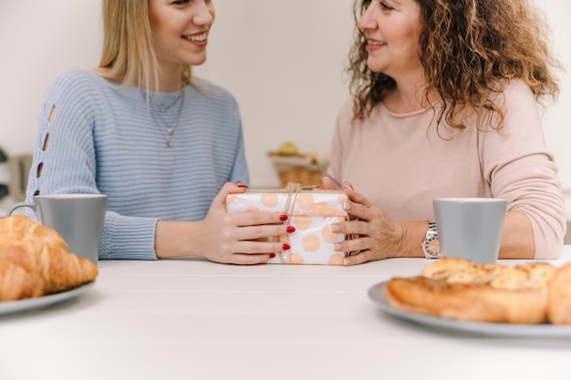 Mujer sonriente dando regalos a mamá durante el desayuno