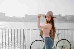 Foto gratuita mujer sonriente delgada en jeans y camisa rosa posando con bicicleta