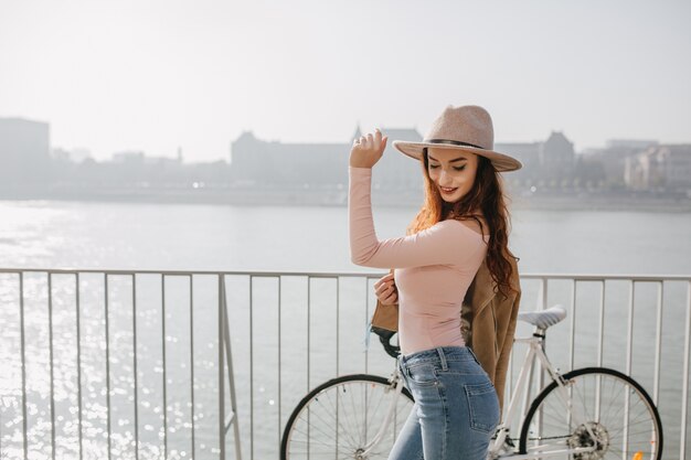 Mujer sonriente delgada en jeans y camisa rosa posando con bicicleta