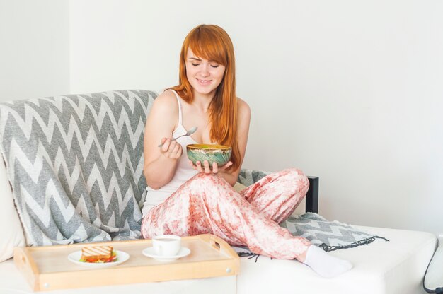 Mujer sonriente desayunando en el sofá