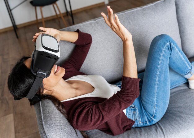 Mujer sonriente divirtiéndose en casa en el sofá con casco de realidad virtual