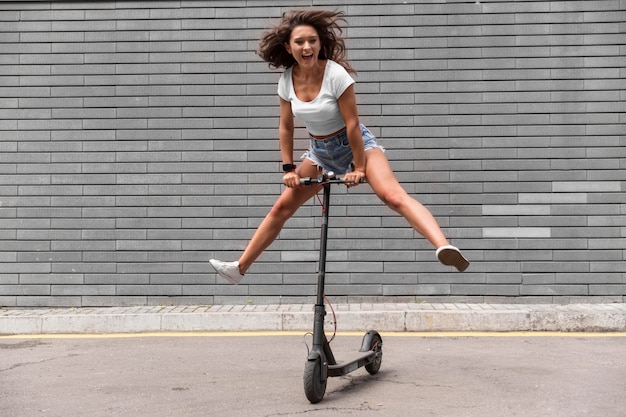 Foto gratuita mujer sonriente divirtiéndose con scooter al aire libre