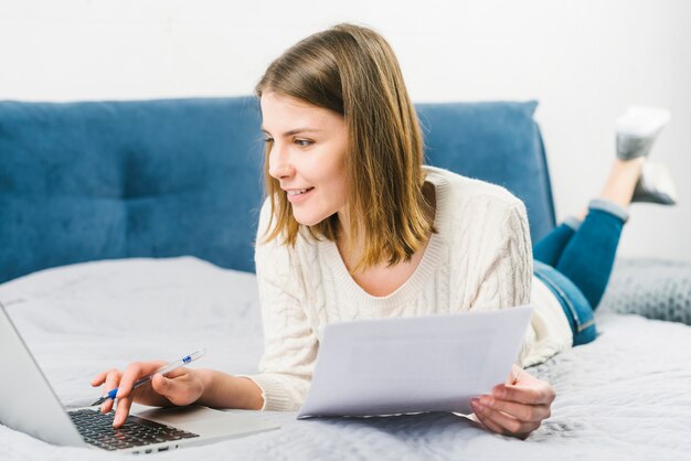 Mujer sonriente con documentos usando laptop