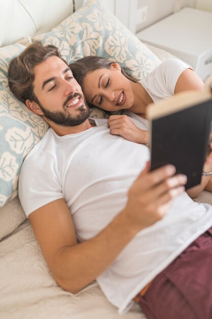 Mujer sonriente durmiendo cerca de hombre de lectura