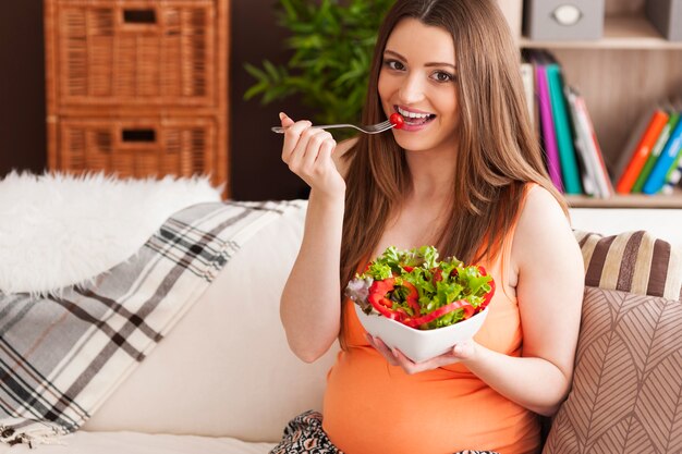 Mujer sonriente embarazada comiendo ensalada