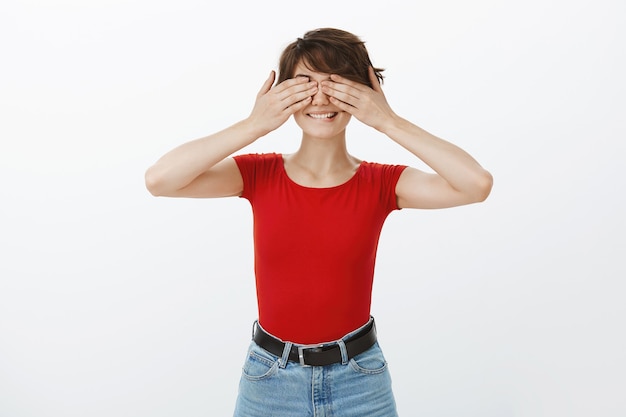 Mujer sonriente emocionada cubre los ojos con las manos, esperando sorpresa, anticipando algo