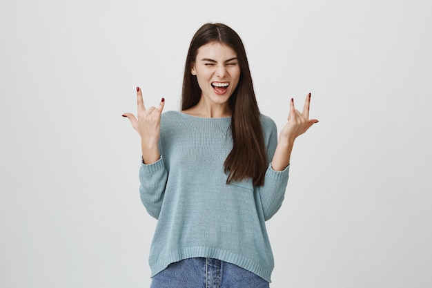 Mujer sonriente emocionada que se divierte, muestra signos de rock-n-roll