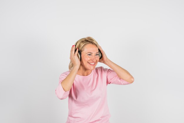 Mujer sonriente envejecida en blusa rosa con auriculares