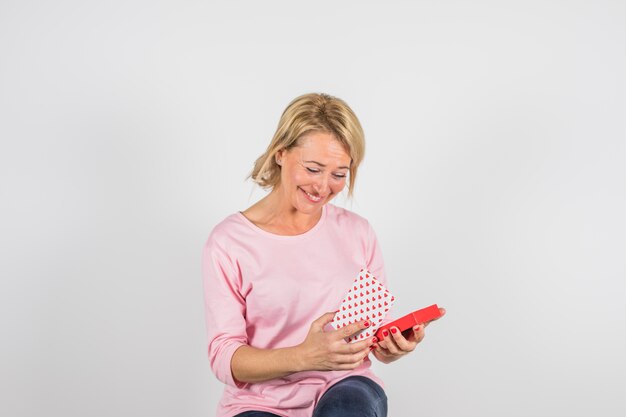 Mujer sonriente envejecida en blusa rosa con caja actual.