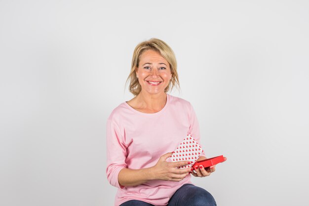 Mujer sonriente envejecida en blusa rosa con caja de regalo.