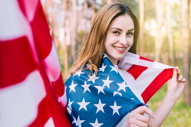 Mujer sonriente envuelta en bandera nacional americana