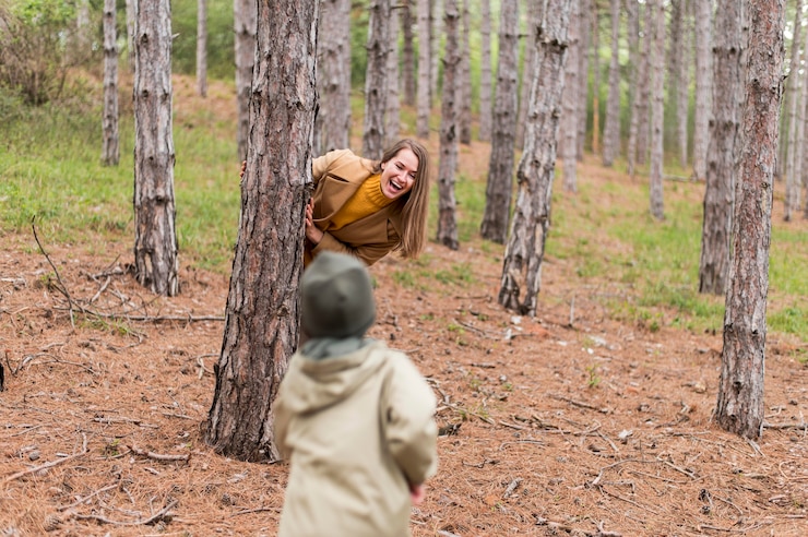 Foto gratuito mujer sonriente escondiéndose detrás de un árbol de su hijo