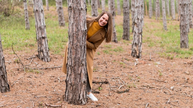 Foto gratuita mujer sonriente escondiéndose detrás de un árbol