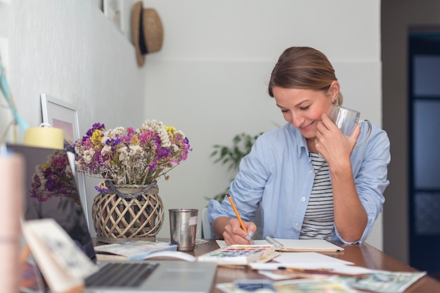 Mujer sonriente escribiendo en el escritorio en el cuaderno