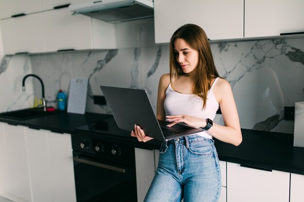 Mujer sonriente escribiendo en su computadora portátil en la cocina