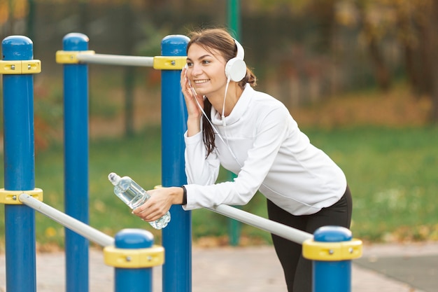 Mujer sonriente escuchando música y sosteniendo una botella de agua