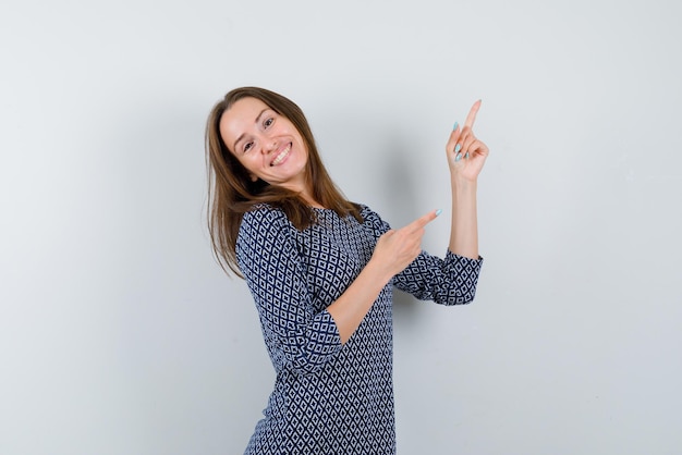 La mujer sonriente está apuntando hacia arriba con los dedos índices sobre fondo blanco.