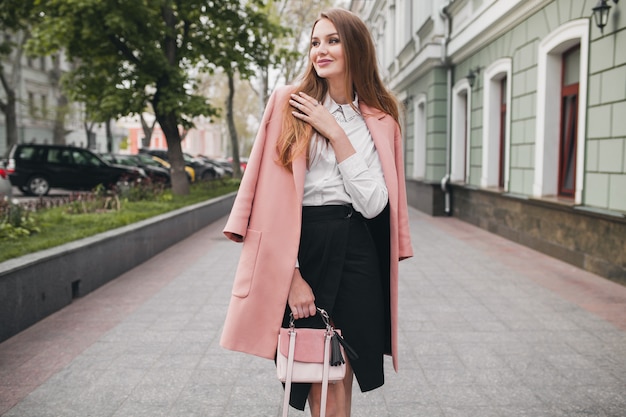 Mujer sonriente con estilo atractivo caminando calle de la ciudad en abrigo rosa