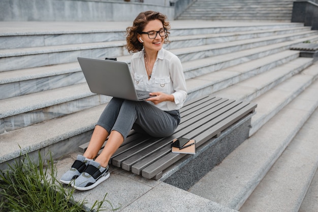 Mujer sonriente con estilo atractivo en gafas trabajando escribiendo en la computadora portátil