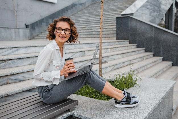 Mujer sonriente con estilo atractivo en gafas trabajando escribiendo en la computadora portátil