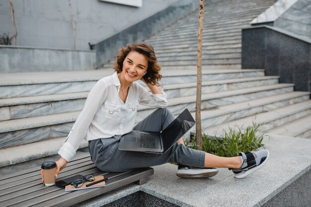 Mujer sonriente con estilo atractivo que trabaja escribiendo en la computadora portátil