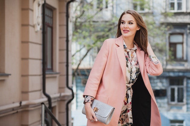 Mujer sonriente con estilo muy atractiva caminando calle de la ciudad en abrigo rosa