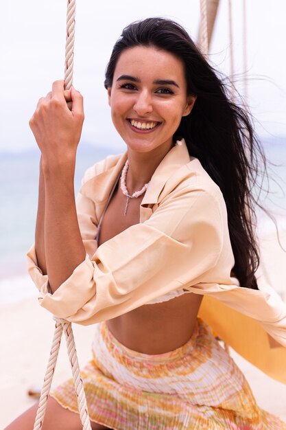 Mujer sonriente feliz en columpio en la playa, luz cálida del día.