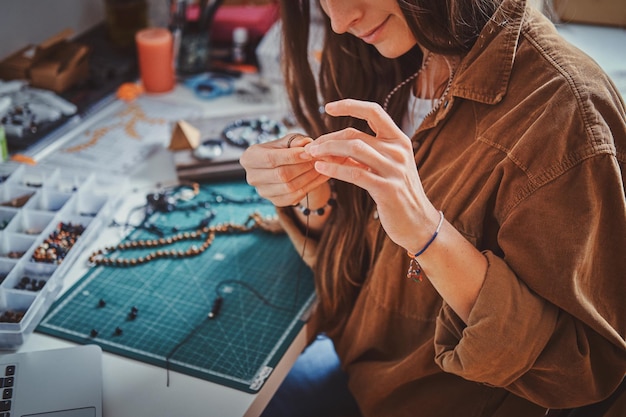 Mujer sonriente feliz está trabajando en joyas de perlas en su propio lugar de trabajo.