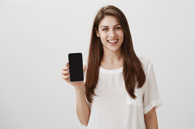 Mujer sonriente feliz que muestra la pantalla del móvil, recomienda la aplicación o el sitio de compras