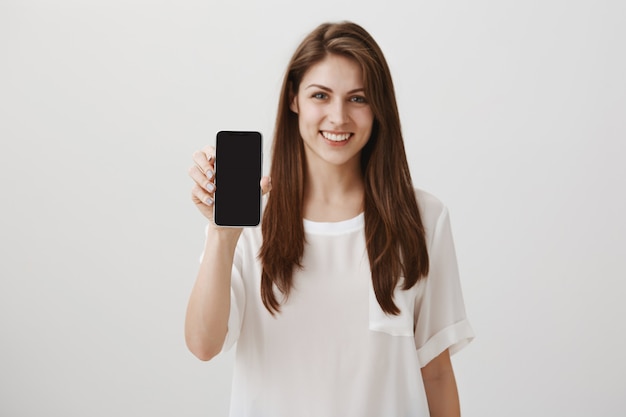 Mujer sonriente feliz que muestra la pantalla del móvil, recomienda la aplicación o el sitio de compras