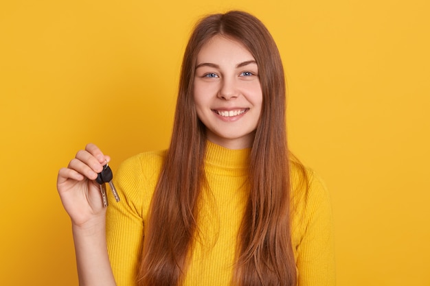 Mujer sonriente feliz que sostiene la llave en las manos, con camisa casual, cabello largo y hermoso, compra un piso nuevo, se ve feliz, expresa emociones positivas, tiene suerte.