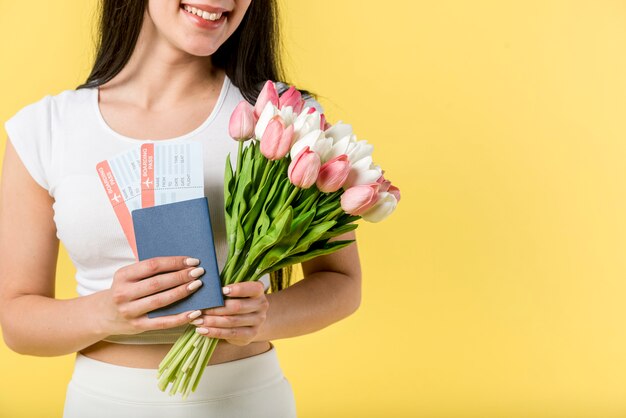 Mujer sonriente con flores y billetes de avión.