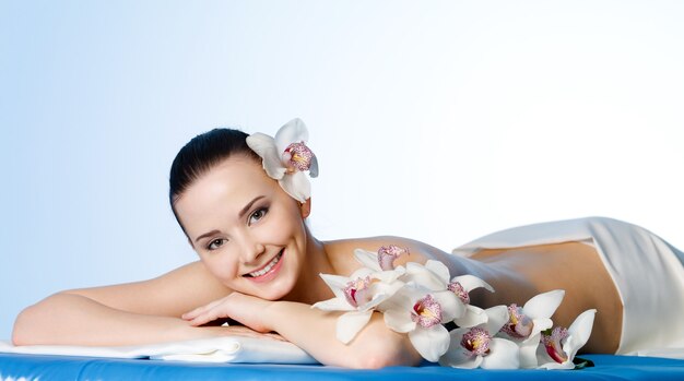 Mujer sonriente con flores descansando en el salón de spa antes del masaje
