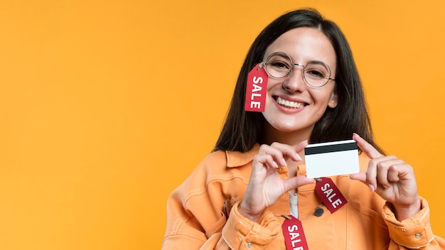 Mujer sonriente con gafas y chaqueta con etiqueta de venta y tarjeta de crédito