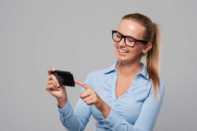 Mujer sonriente con gafas mediante teléfono móvil