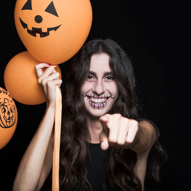 Mujer sonriente con globos de Halloween apuntando hacia ti