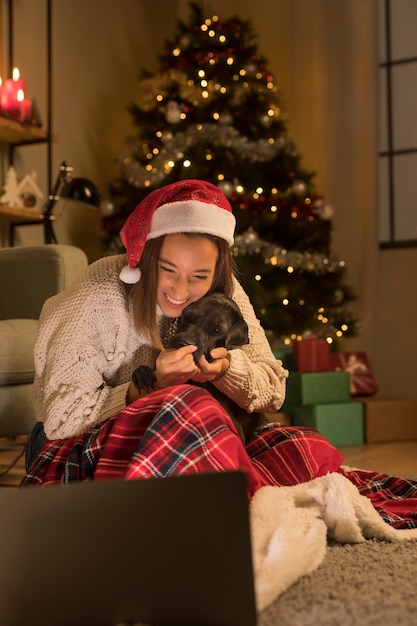 Mujer sonriente con gorro de Papá Noel y su perro mirando portátil en Navidad