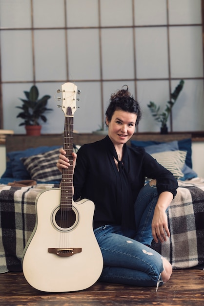 Mujer sonriente con guitarra en su habitación