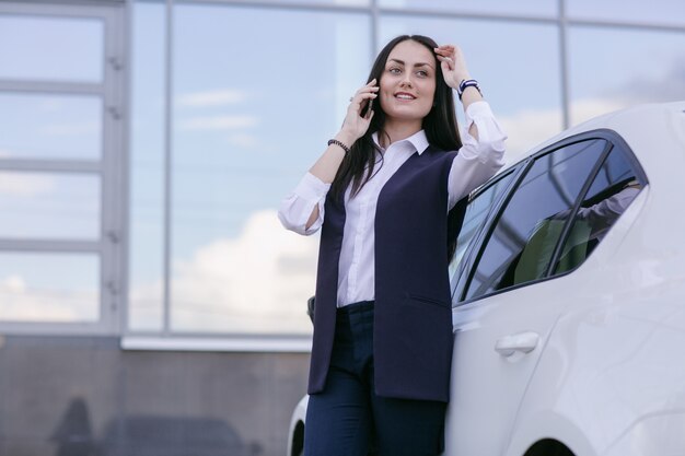 Mujer sonriente hablando por teléfono apoyada en un coche