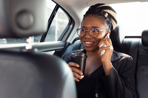Mujer sonriente hablando por teléfono en el asiento trasero del coche mientras toma un café