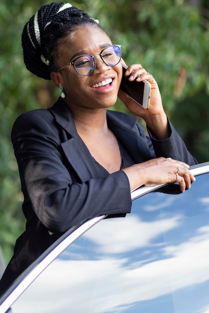 Foto gratuita mujer sonriente hablando por teléfono inteligente mientras se inclina contra la puerta de su automóvil