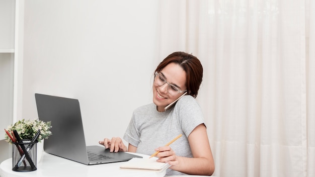 Mujer sonriente hablando por teléfono mientras trabajaba en la computadora portátil