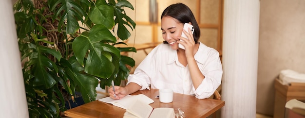Foto gratuita mujer sonriente hablando por teléfono móvil, contesta una llamada y parece feliz sentada en un café