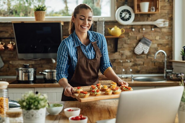 Mujer sonriente haciendo un blog de cocina y mostrando bruschetta saludable que ha preparado en la cocina