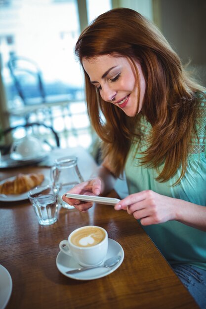 Mujer sonriente haciendo clic en la foto de café desde el teléfono móvil