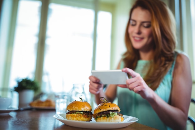 Foto gratuita mujer sonriente haciendo clic en la foto de la hamburguesa del teléfono móvil