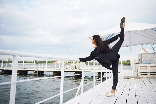 Mujer sonriente haciendo ejercicio de yoga al aire libre en el muelle de la playa.