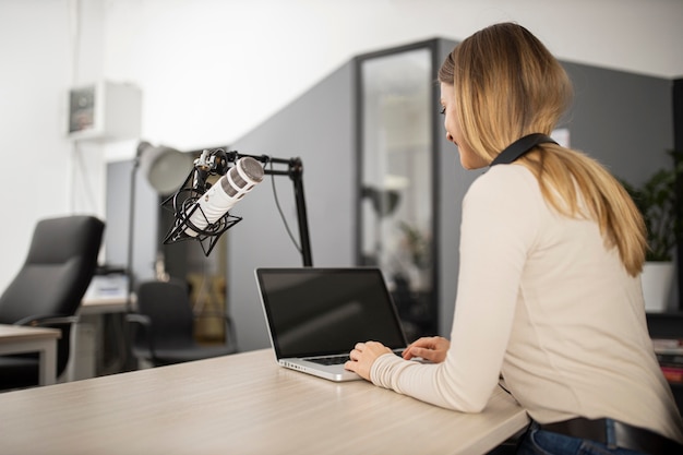 Mujer sonriente haciendo radio con laptop y micrófono